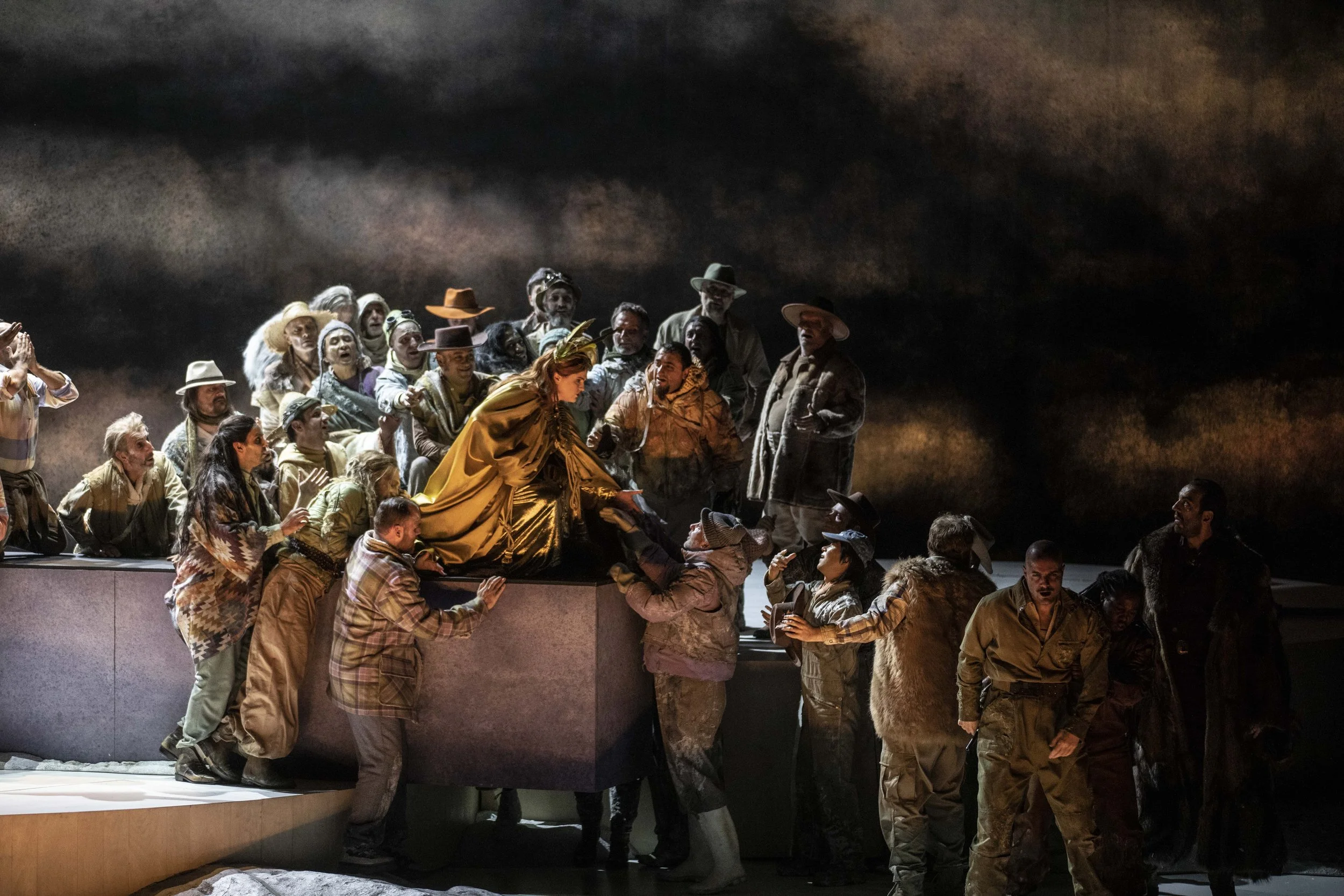 Theaterstück mit vielen Schauspielern auf einer Bühne, die in historischen Kostümen auftreten, vor einem dunklen Himmel.