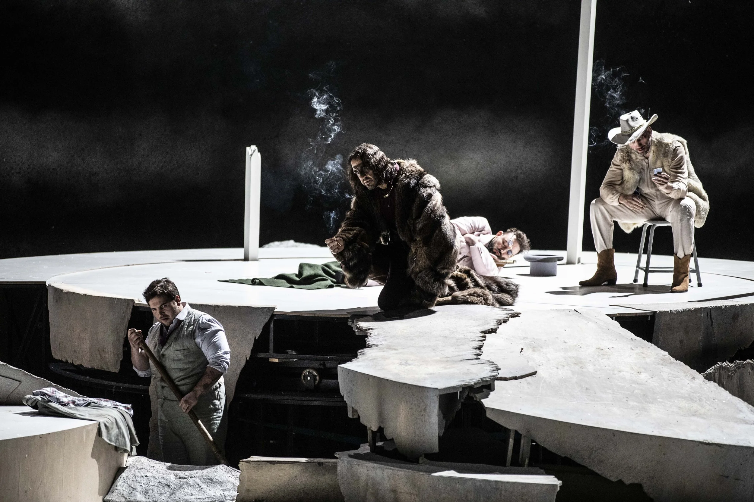 Theaterbühne mit vier Schauspielern in Kostümen, aufgeteilt in verschiedene Ebenen und Plattformen, mit dunklem Hintergrund und Rauchschwaden.