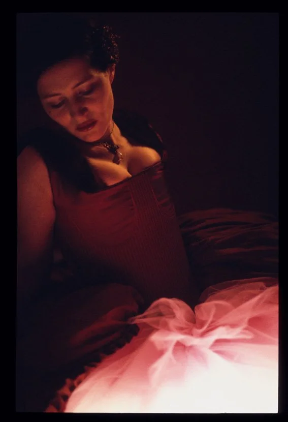 Frau in dunklem Raum mit Kerzenschein, trägt rotes Kleid und Schmuck, schaut nach unten, entspannt.