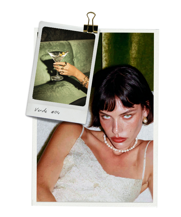 A woman with dark hair and light skin lying down in a sparkly dress, wearing a pearl necklace and earrings, looking at the camera. There is a polaroid picture clipped on black background showing a hand holding a martini glass with an olive, resting on a green sofa. The polaroid has the handwritten text "Verde #04."