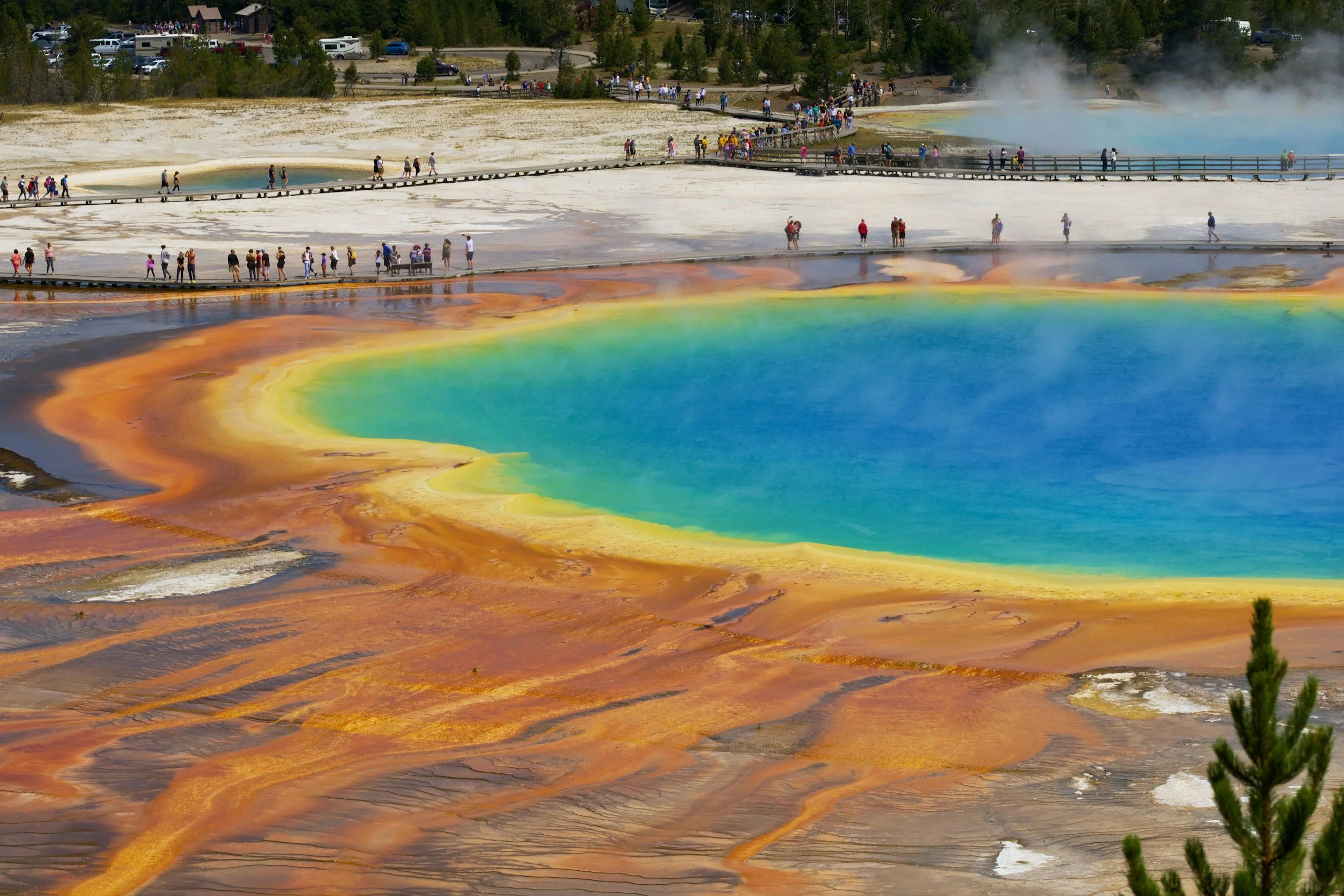 Colorful thermal pool at Yellowstone with steaming water, walkways, and many tourists visiting in a national park.