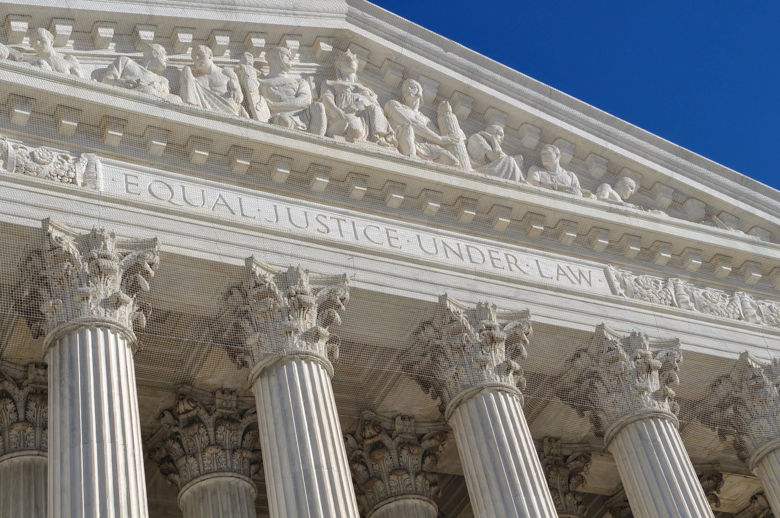 Close-up of the U.S. Capitol building's ornate exterior featuring statues, columns, and detailed friezes, with a clear blue sky in the background.