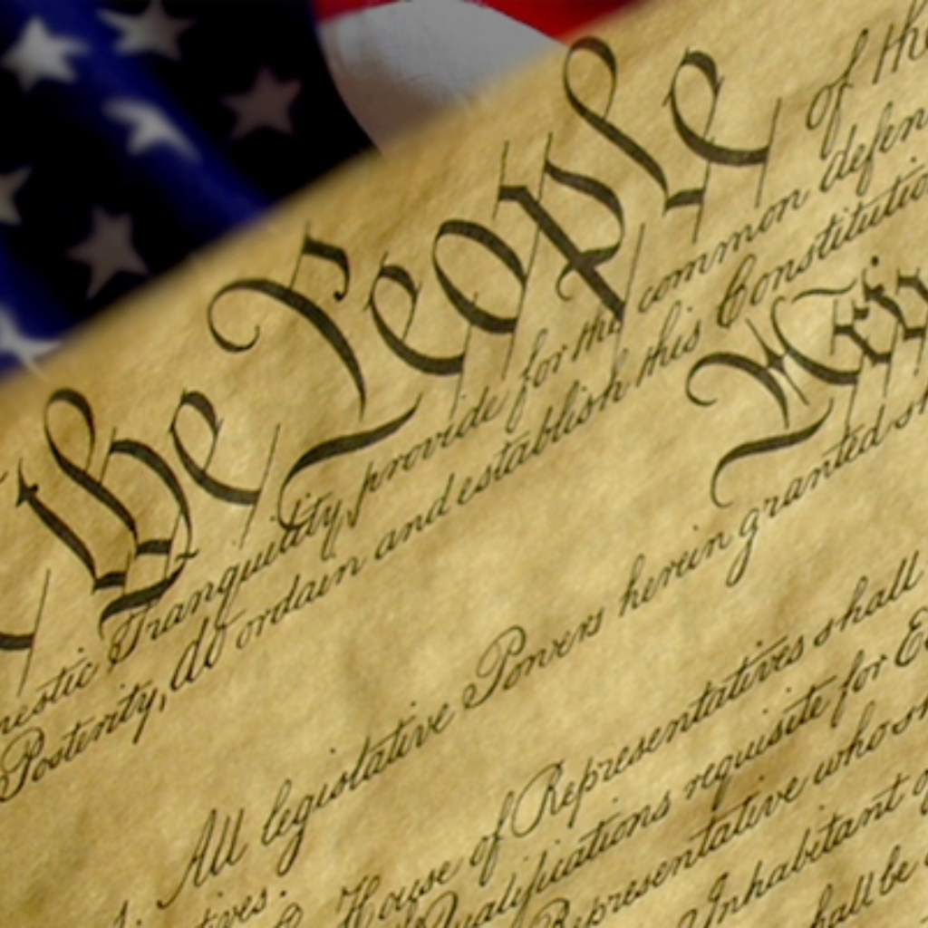 Close-up of the United States Constitution with an American flag in the background.