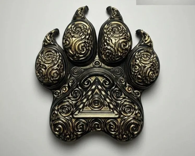 Decorative black and gold animal paw-shaped design with swirling patterns and an eye inside a triangle.
