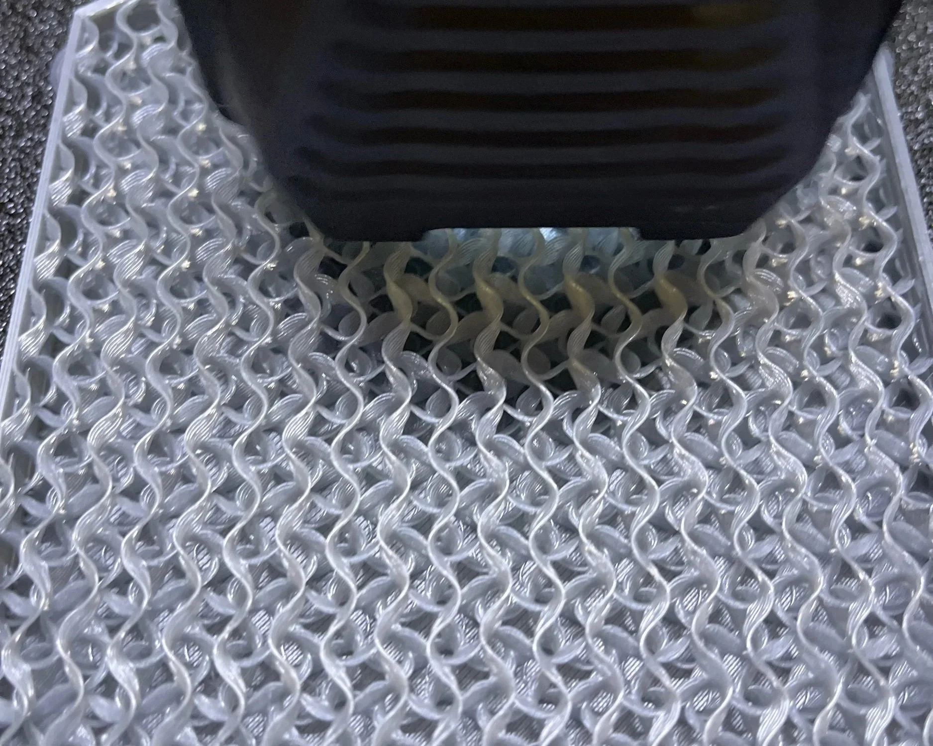 Close-up of a textured metal grate with a black object pressing down on it.