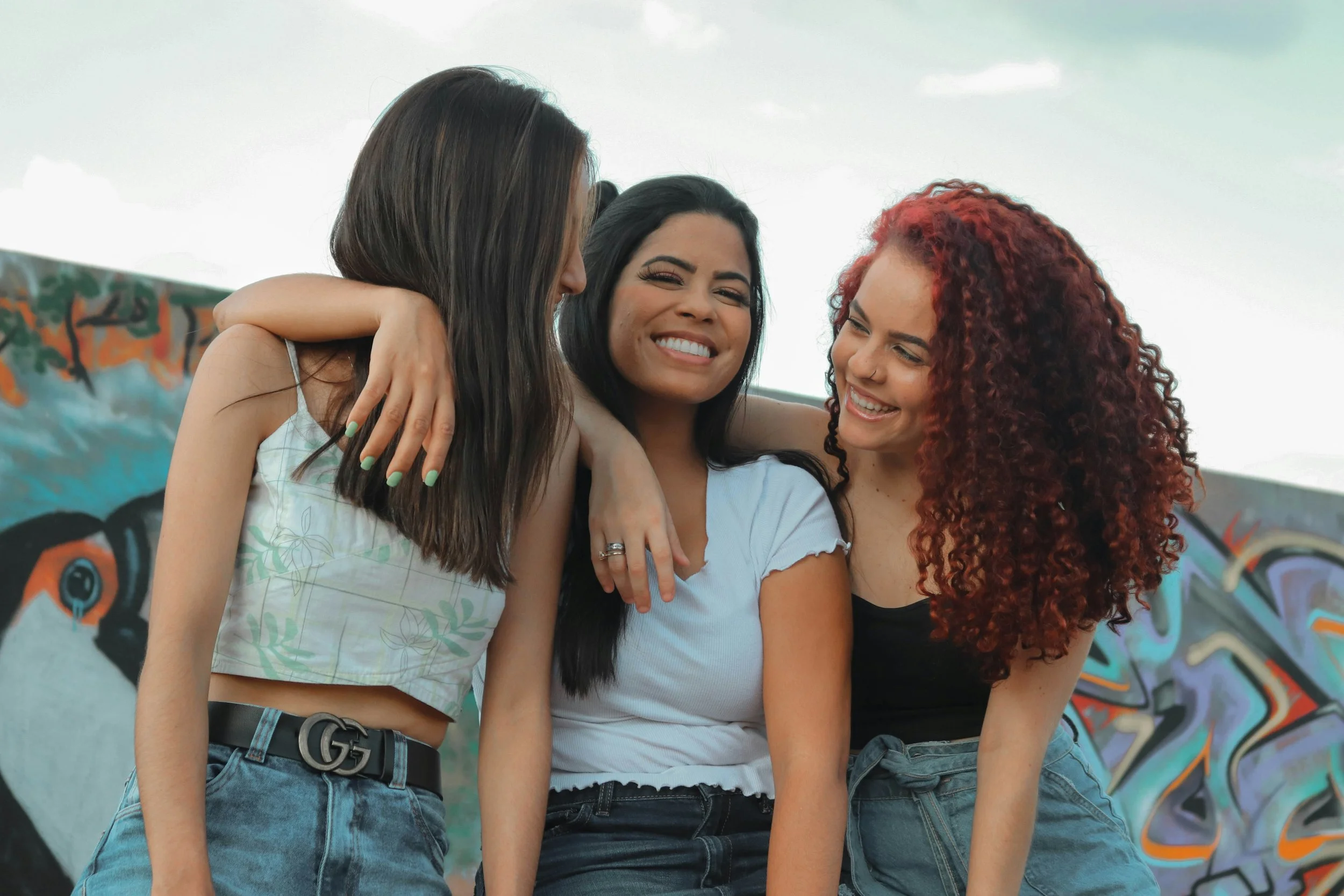 Three polyamorous partners smiling together with their arms around each other, representing connection, affection, and supportive relationships.