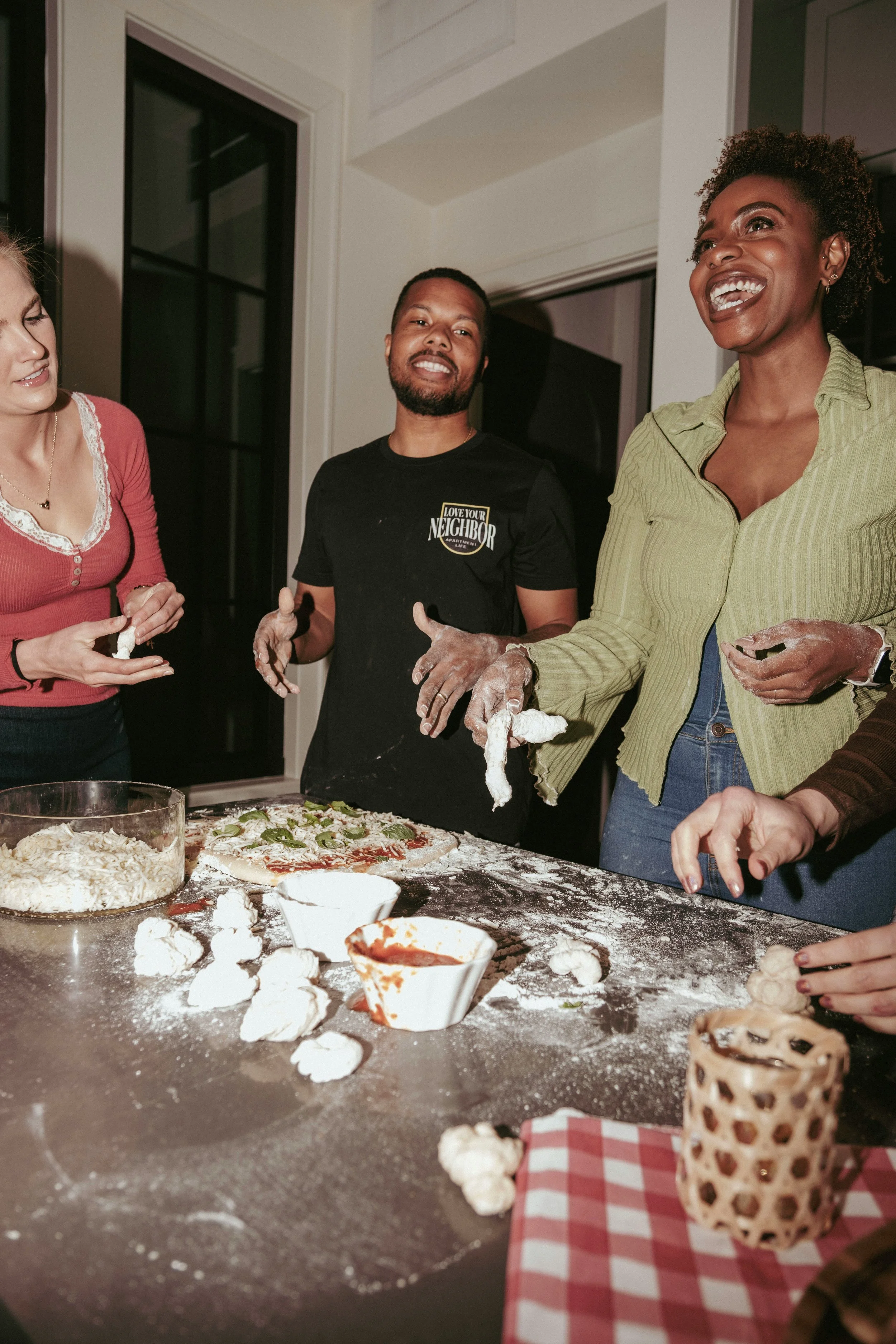 Three partners cooking pizza together, laughing and enjoying connection, teamwork, and shared relationship moments.