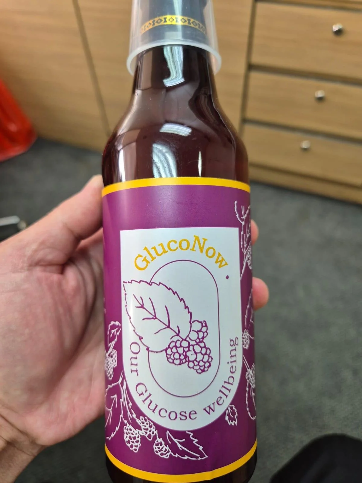 A bottle of Glucono, a health supplement promoting glucose and wellbeing, featuring a purple label with a leaf and berries illustration.