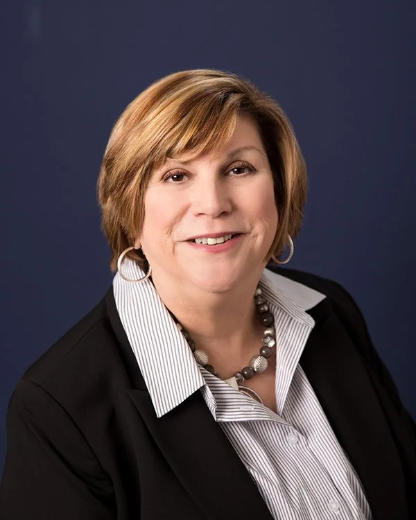Professional portrait of a smiling middle-aged man in a dark suit, white shirt, and red tie, against a plain background.