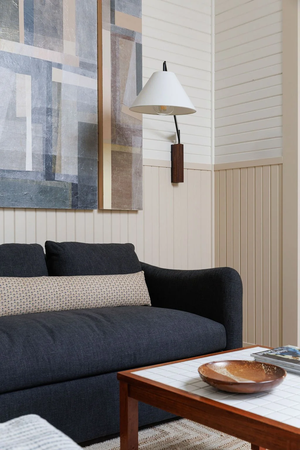 Sofa with wall lamp and art on wall - coffee table with bowl and magasines on top. .