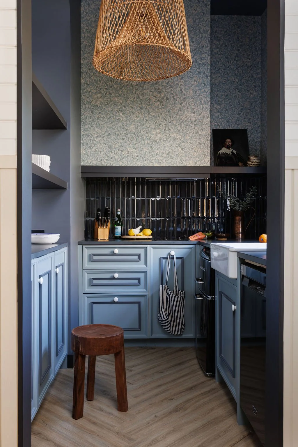 Dark blue Selby Hotel kitchen with shiny tile back splash, blue cabinetry and blue floral wallpaper.
