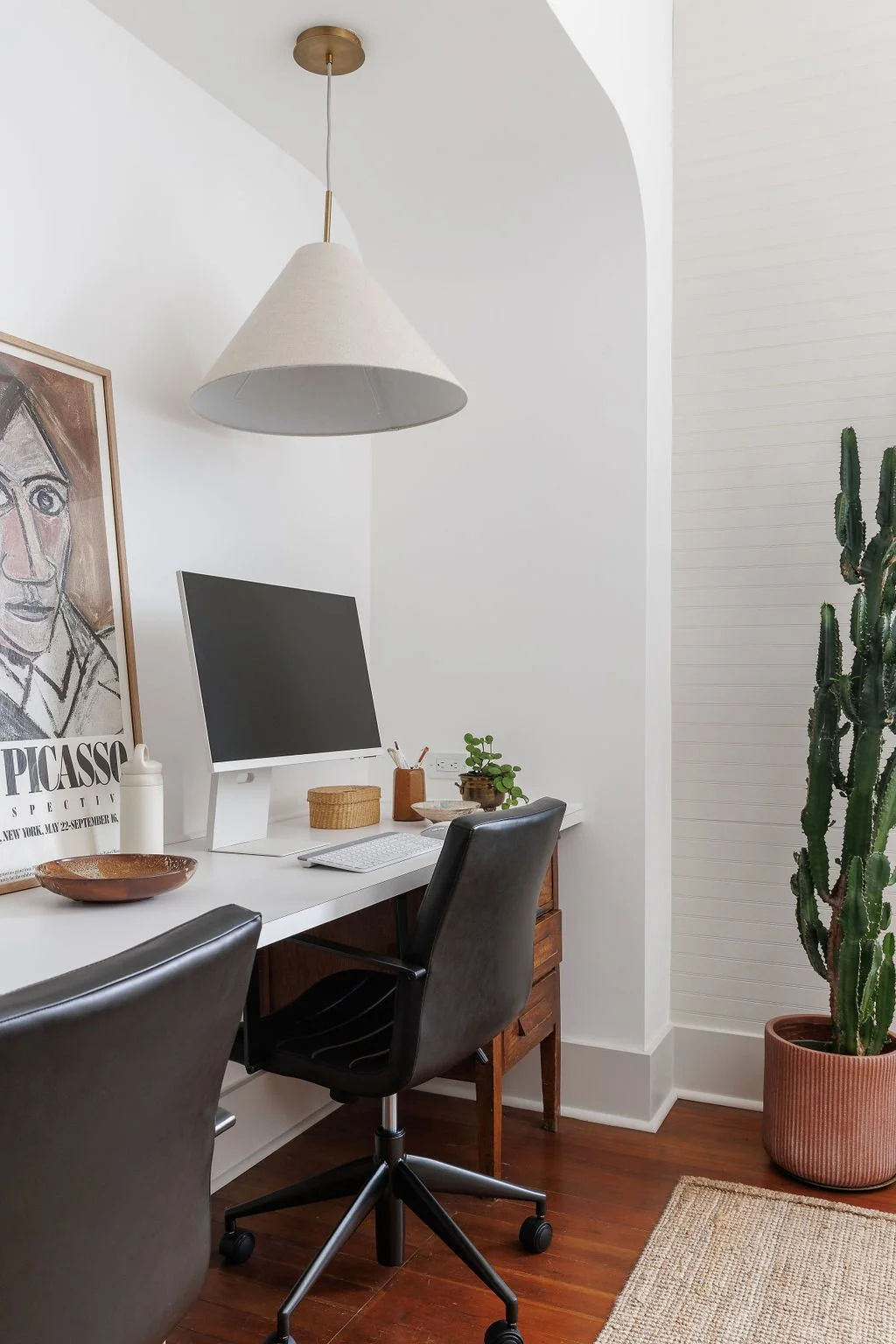 Office desk with stylish white office decor, black office chairs, Picasso art print and cone linene pendant in arched bulkhead above desk.
