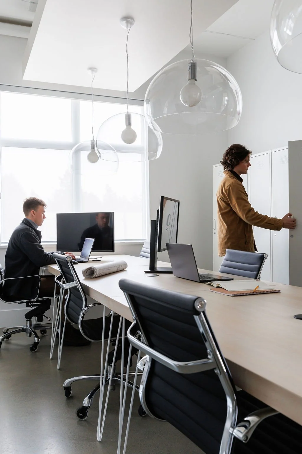 Photo of two men working in an office space, one man is opening a locker. 