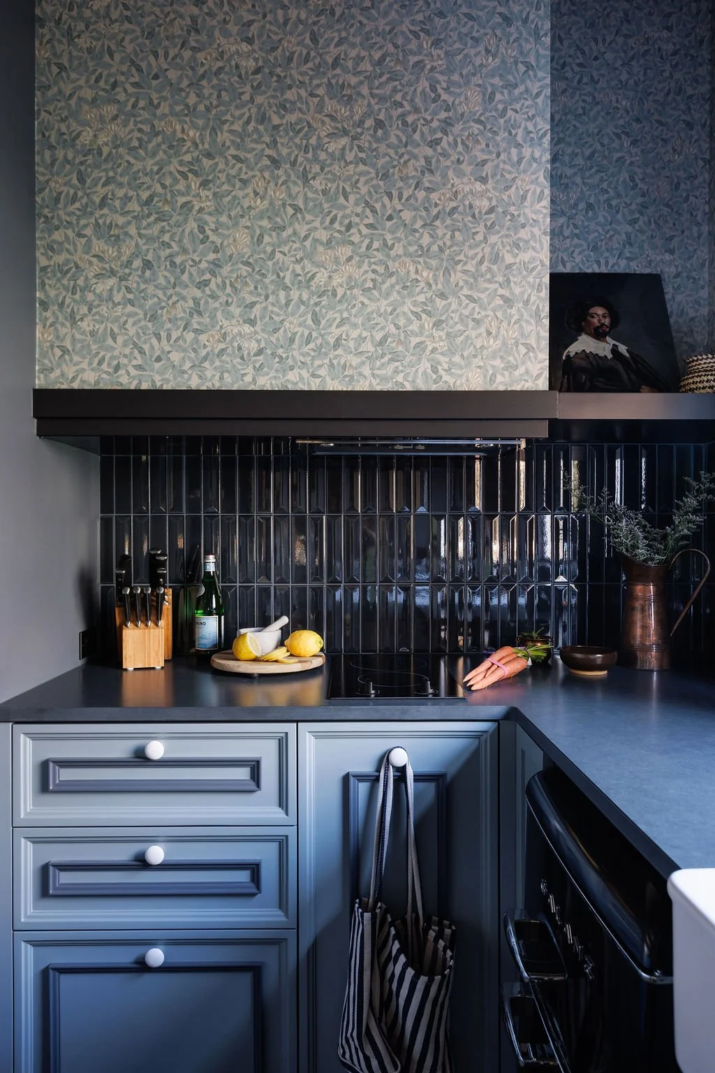 Dark blue Selby Hotel kitchen with shiny tile back splash, blue cabinetry and blue floral wallpaper.