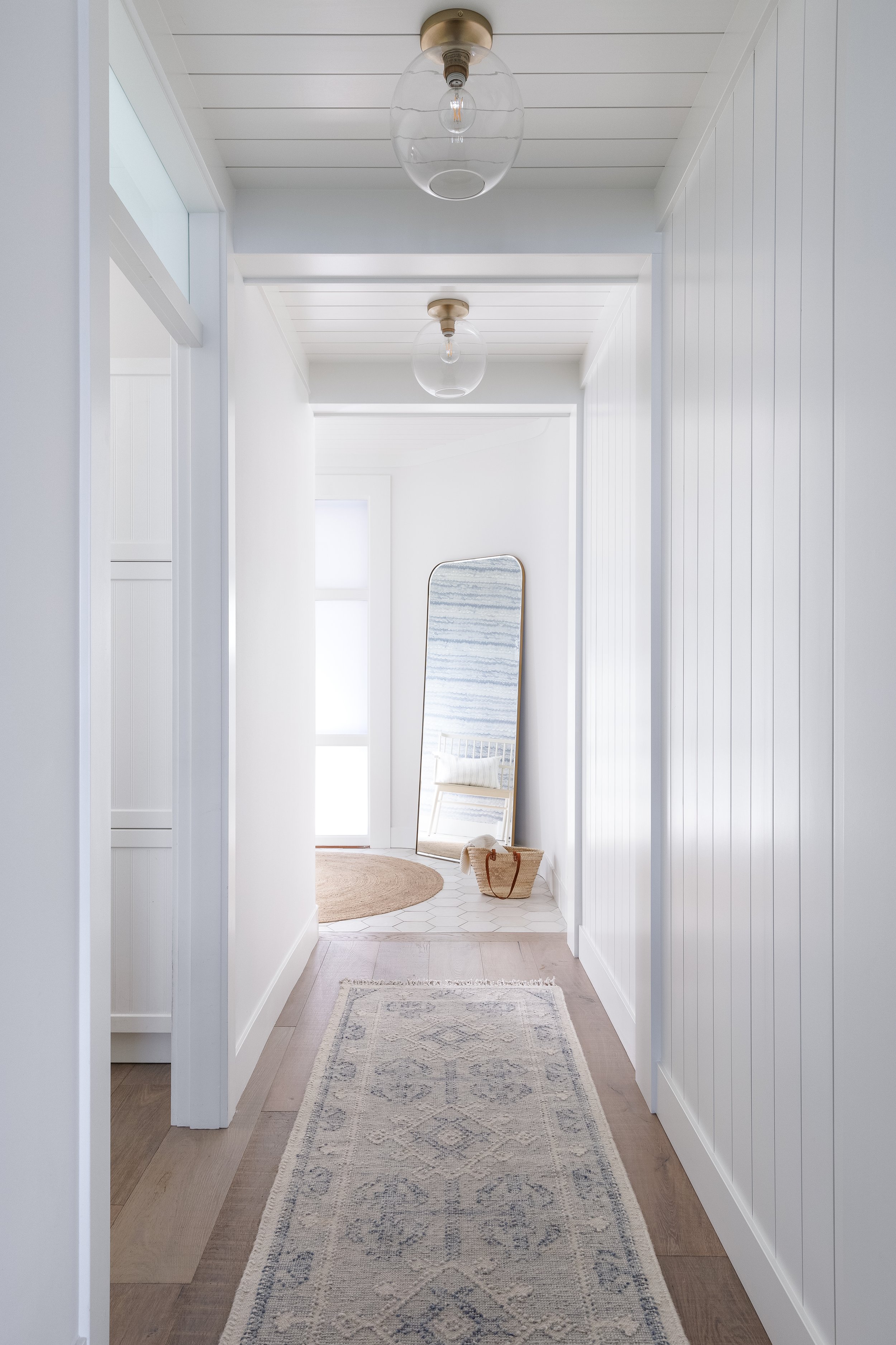 Hallway with rug looking towards mirror in sun-lit entry.