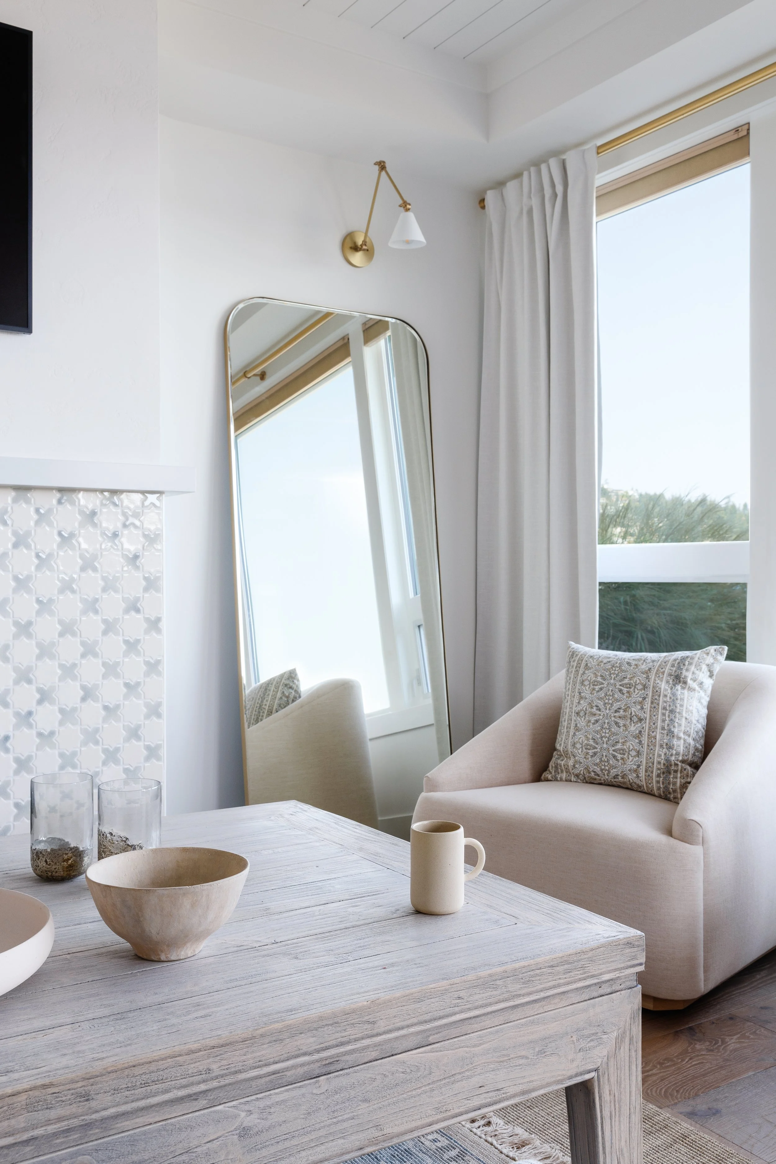 White swivel chair next to reflective tall mirror with wall sconce above.