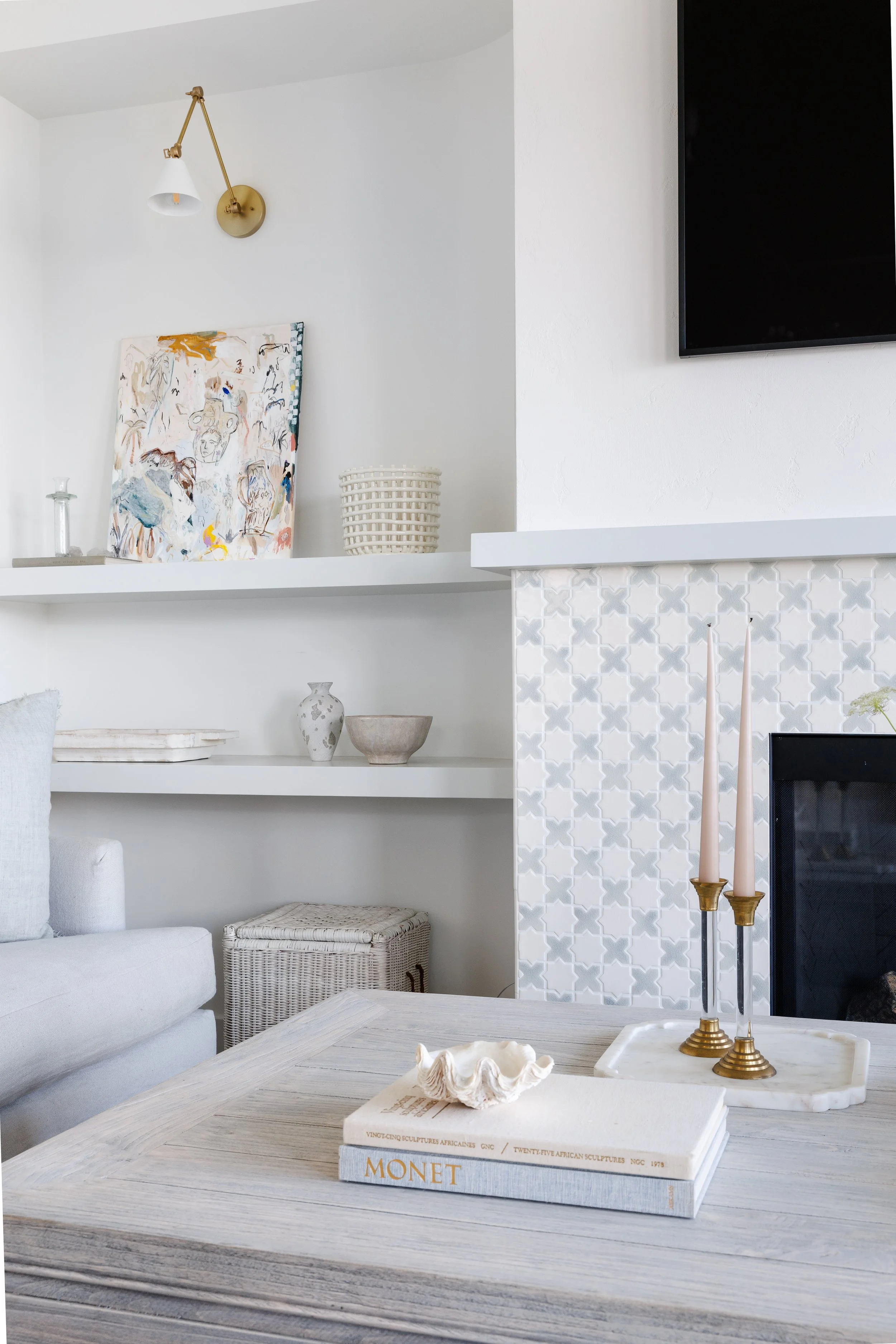 Close-up picture of fireplace with pretty white and blue mosaic tiles. Floating shelf next to fireplace with art and decor creatively displayed.