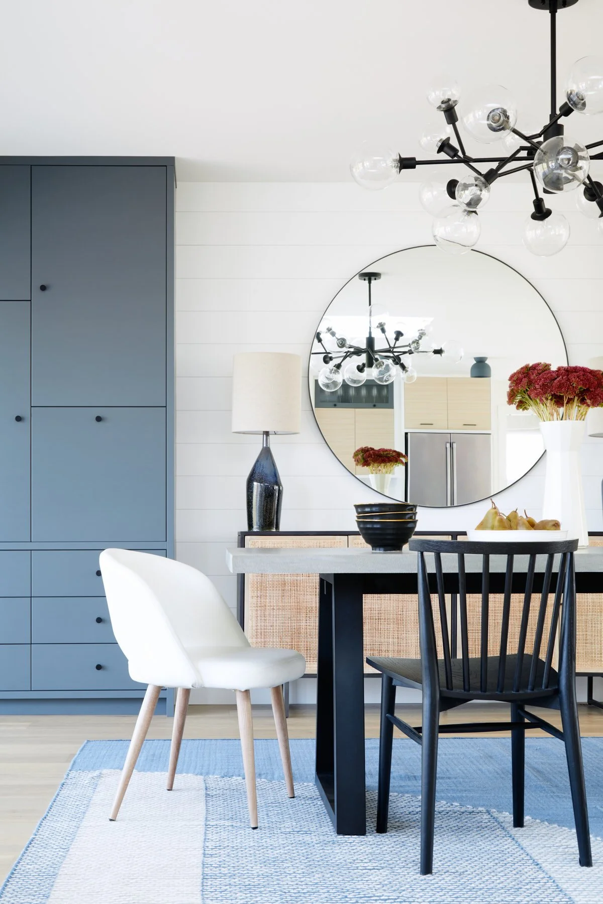Photo of dining table and chair with blue cabinetry and mirror behind table, decor on table. 