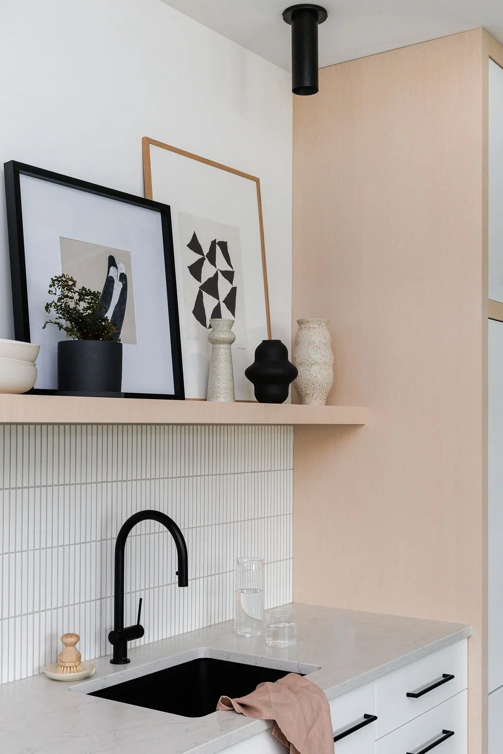 Close-up angle of kitchen, wooden shelving, with graphic art, white mosaic and black plumbing.