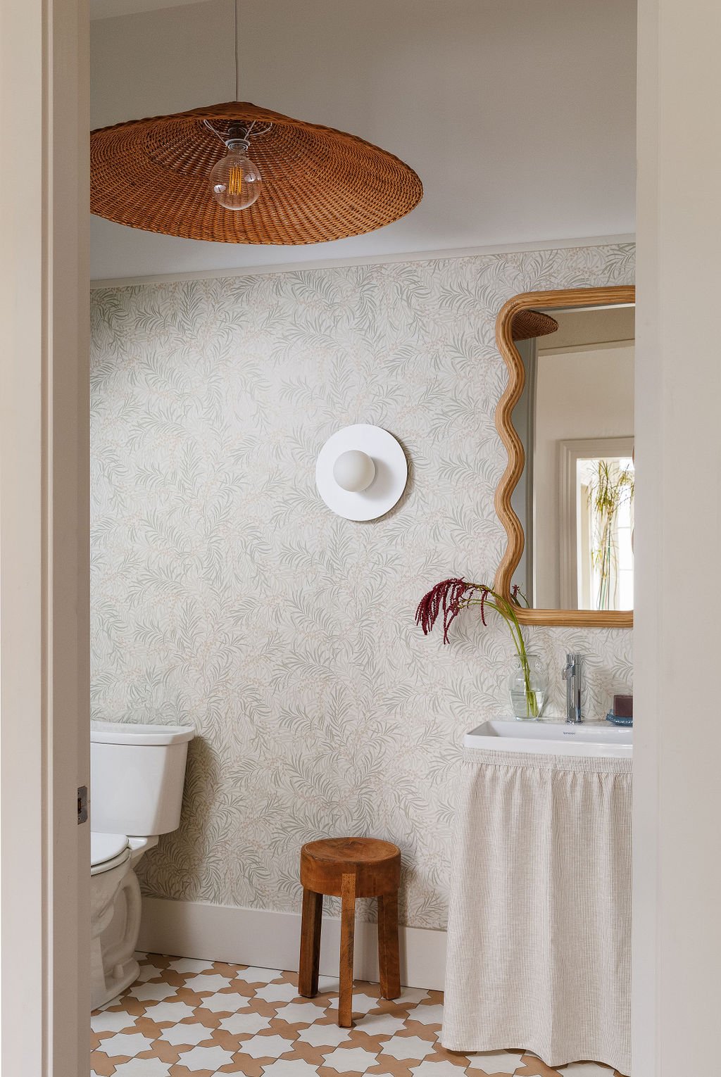 Looking through door into washroom with skirted vanity and wave mirror and large wicker pendant light.