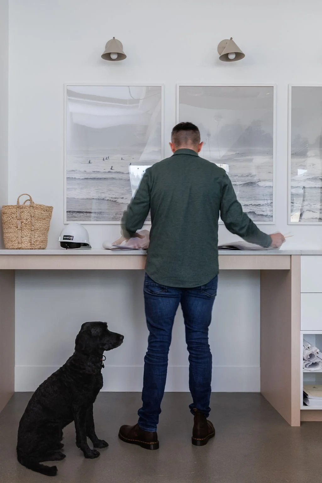 Photo of man looking at plans at stand up desk, black dog sits beside man.