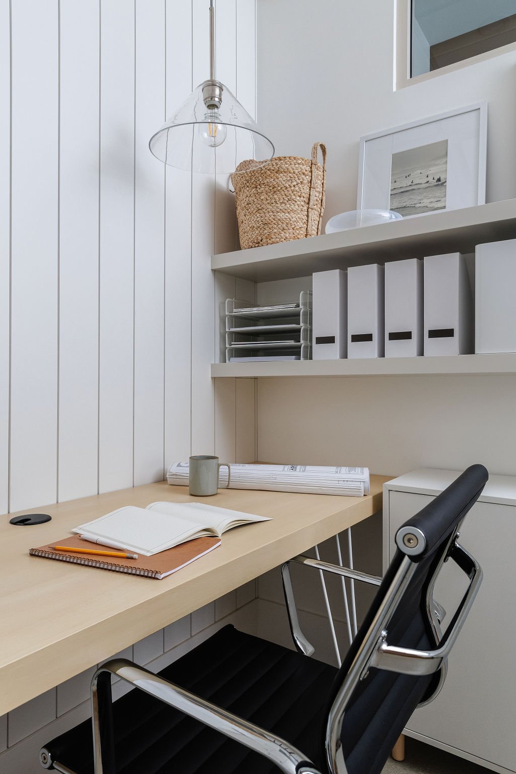 Photo of stylish white office with wood desk top and floating shelving with functional decor.