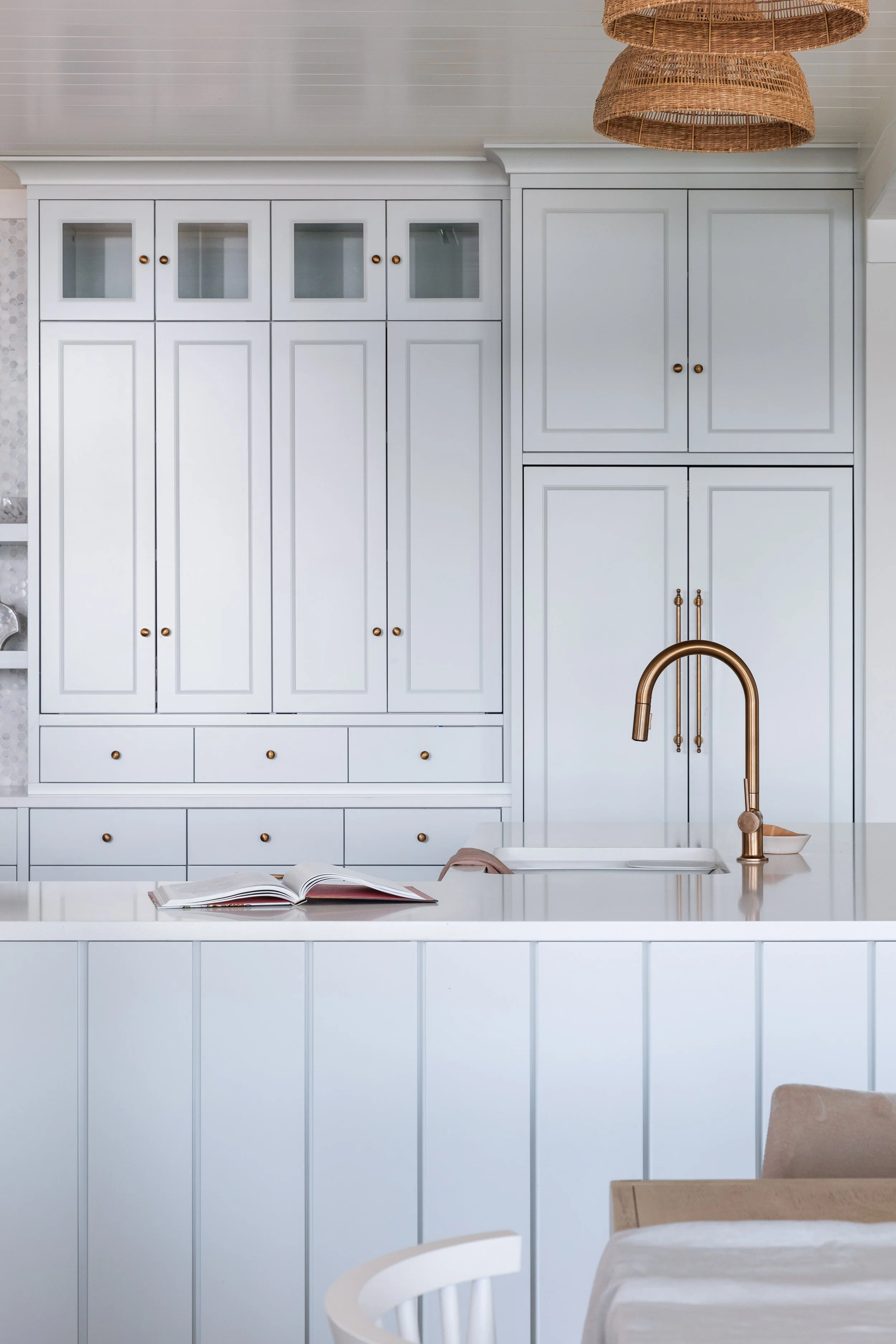 Light blue tower cabinet cabinetry with gold hardware, white counter and gold faucet. 