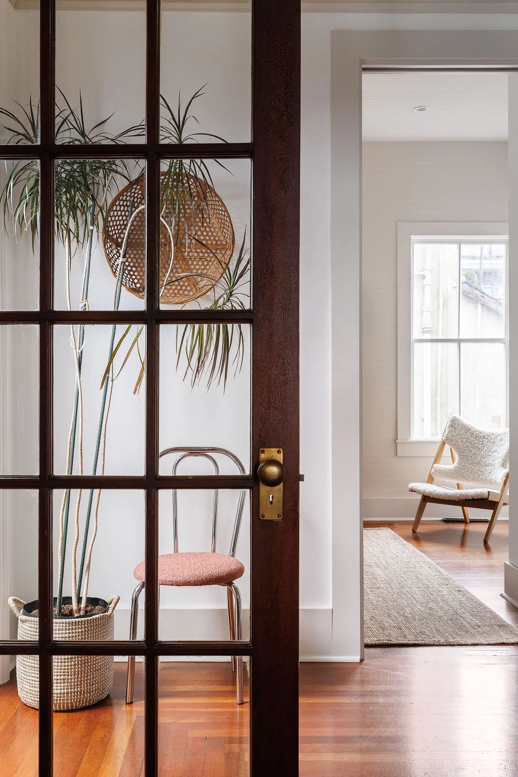 Looking through mahogany and glass French door at cafe chair, plant and woven rattan art on wall.