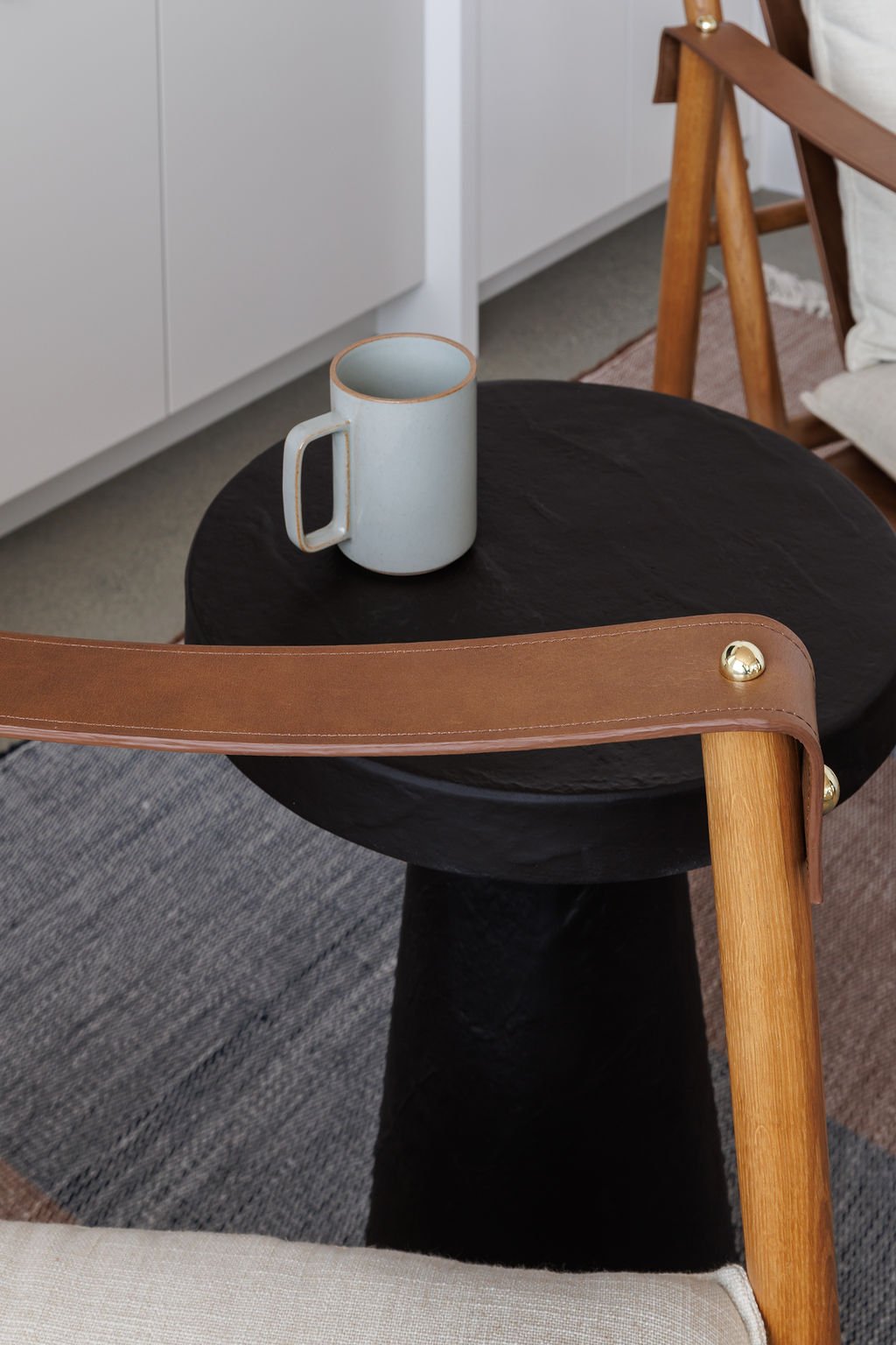 Close-up photo of black side table with coffee cup and leather arm of chair.