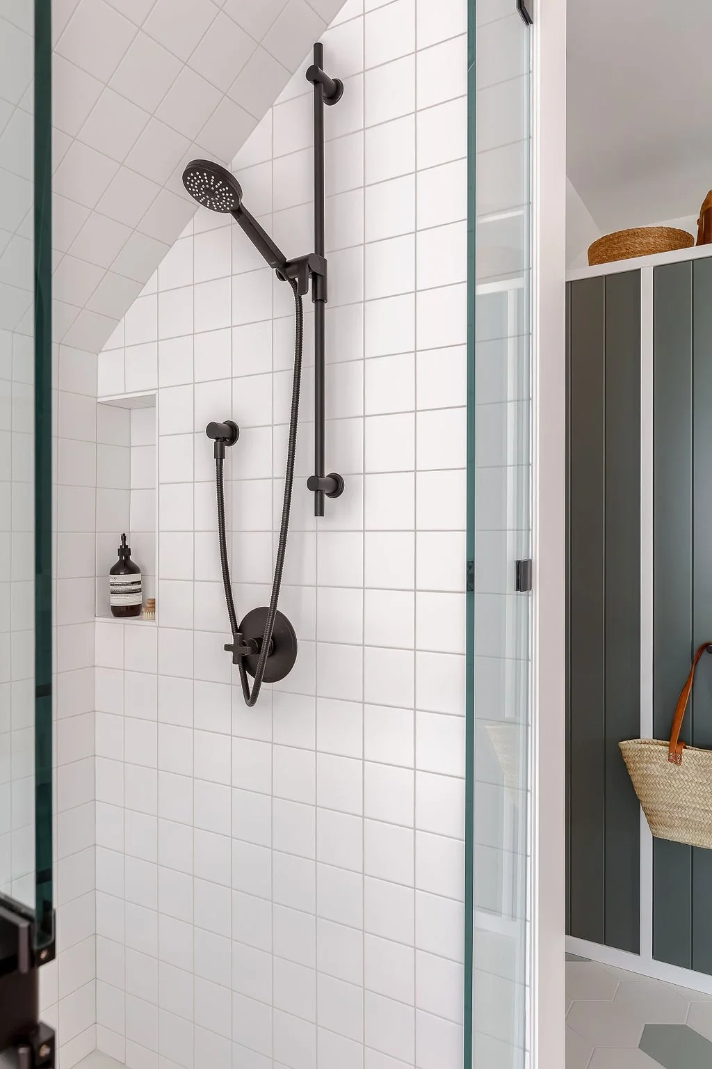 White square tiles in shower with black plumbing hardware and soap niche.