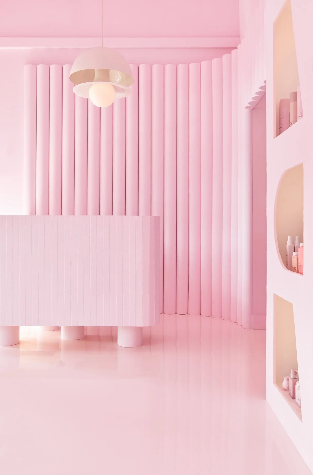 Pink Label hair salon front entry desk service counter with textural feature wall behind. The space feels bring and vibrant.
