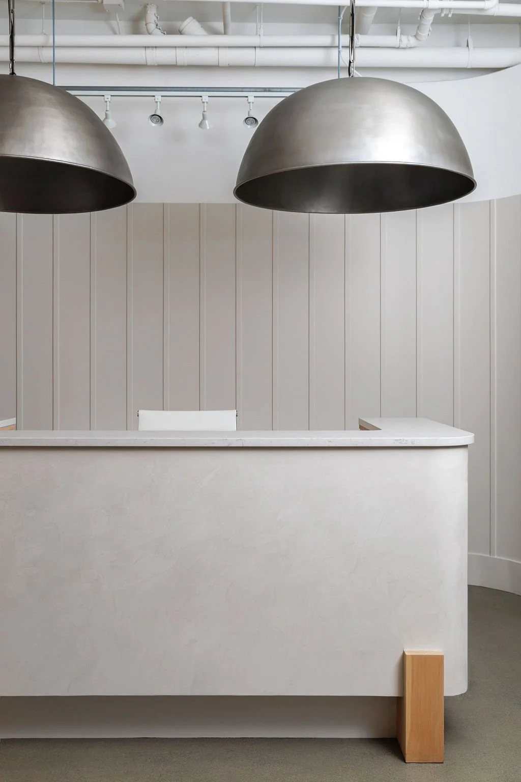 Photo of office entry withy curved plaster reception desk with large dome pendant lights over desk.