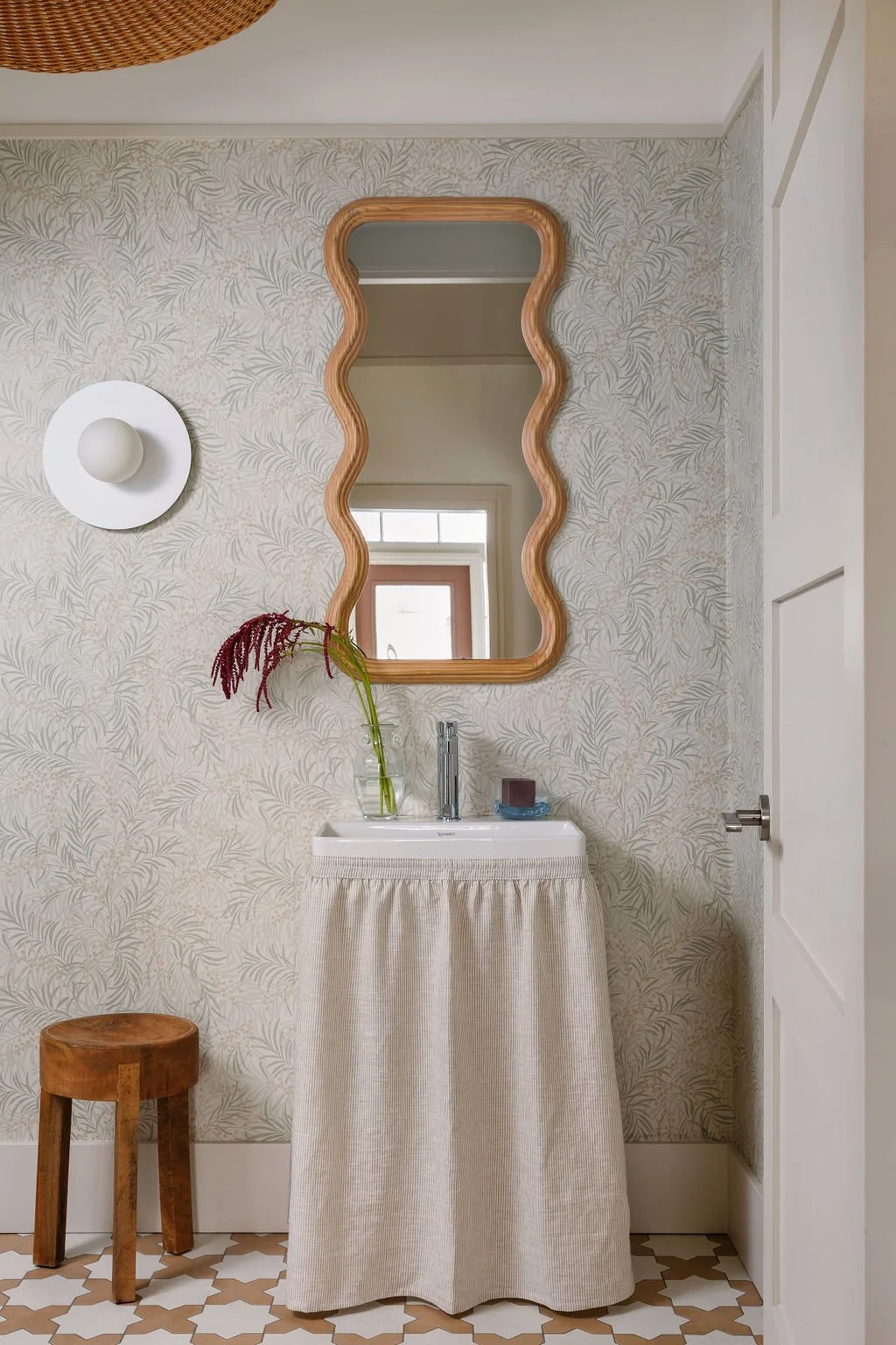 Looking through door into washroom with skirted vanity and wave mirror.