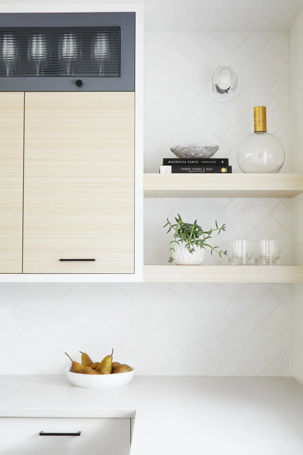 Close-up photo of white kitchen with decor on floating shelf with sconce light above.