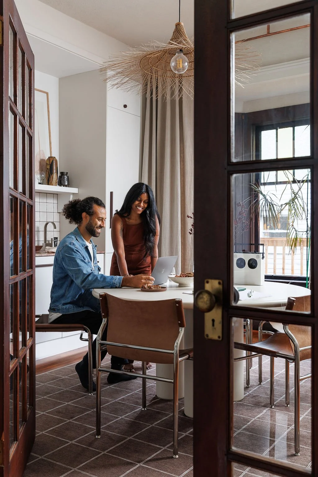 Siya and Rasila Herman happily working at white dining boardroom table surrounded by rich wood French doors.