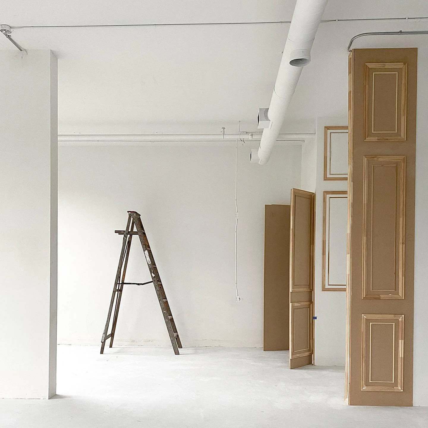 Interior room under construction with a stepladder, beige cabinets, and white walls and ceiling.
