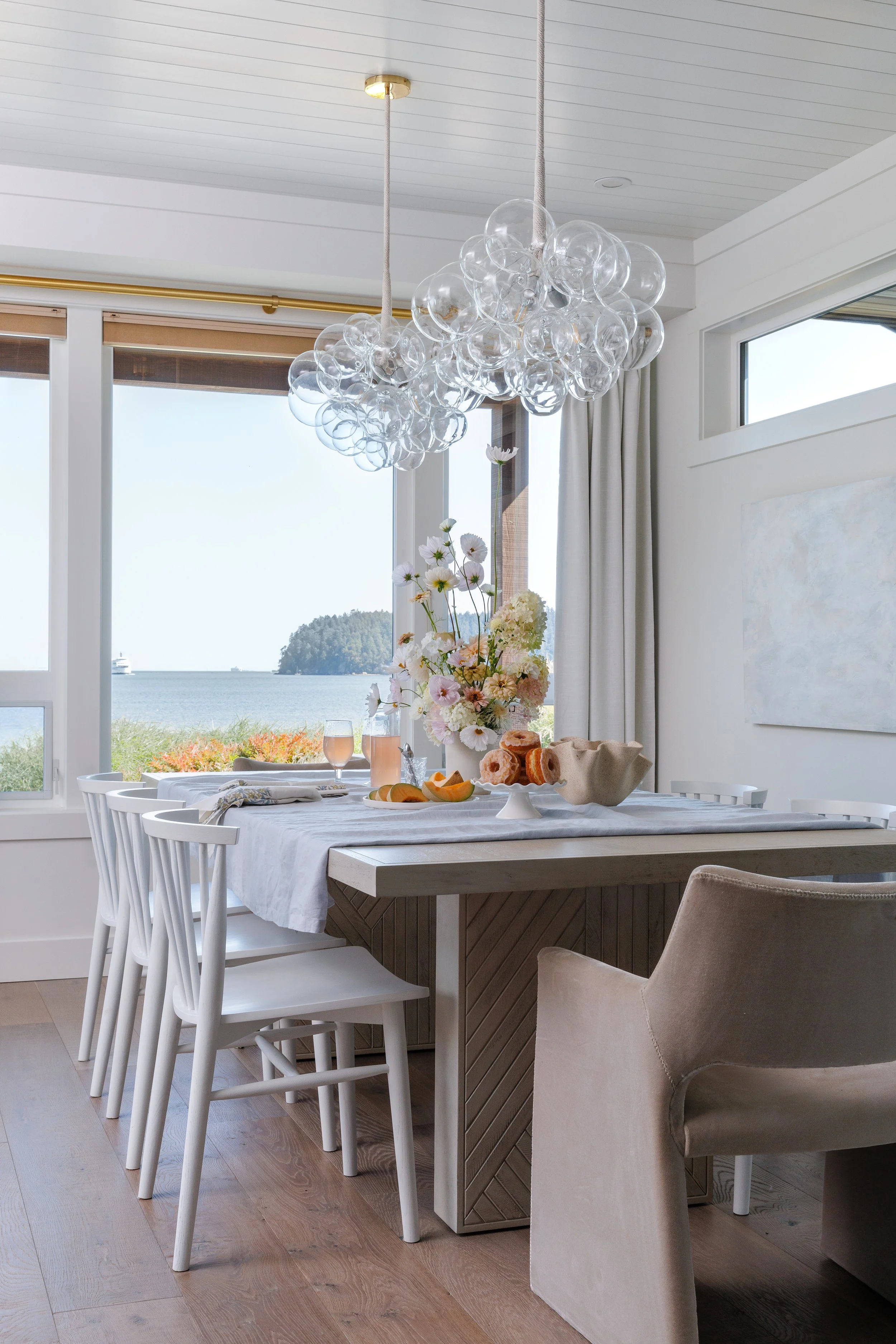 Wood dining table with linen table cloth, decor, spring flower aroangment and decor on table. Vew out to ocean from dining room.