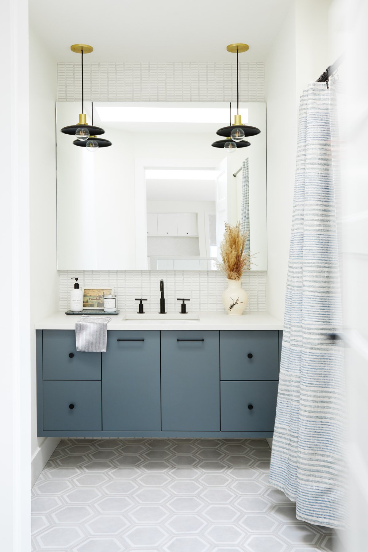 Photo of blue washroom vanity wall with mirror, black pendant lighting and black hardware and plumbing. 