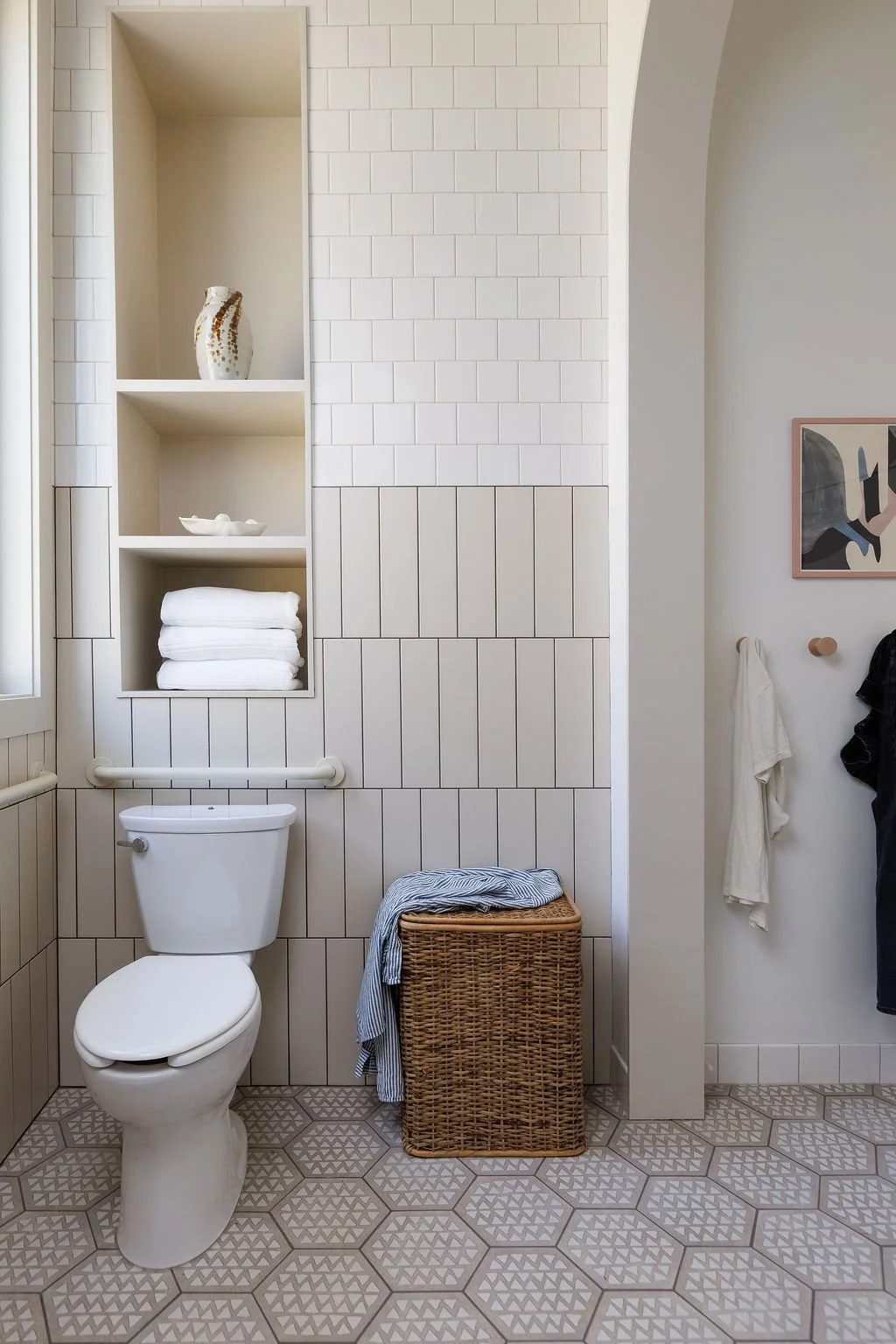 Toilet with shelving niche above and hooks on wall with clothing.