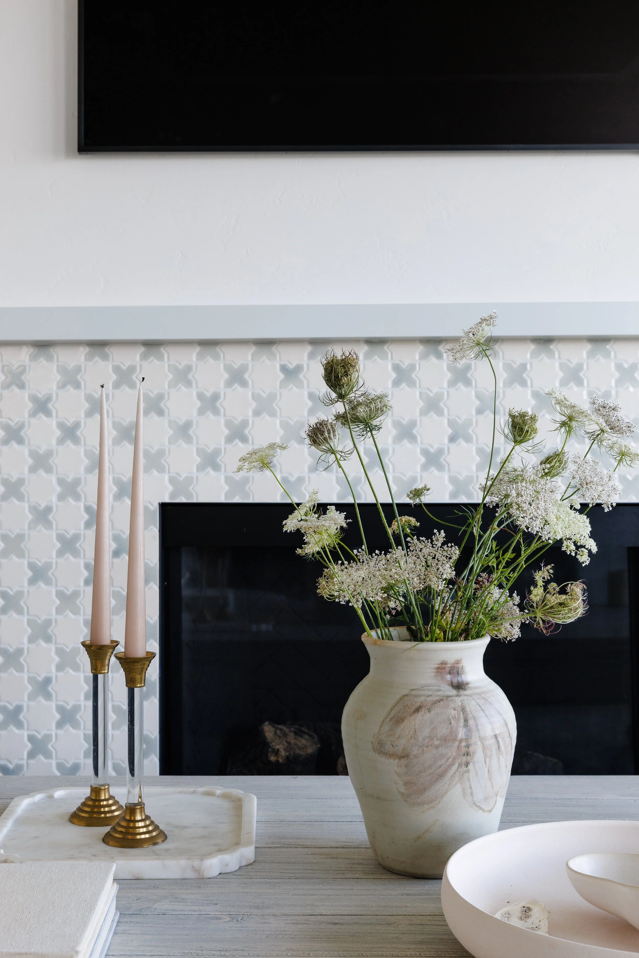 Close-up of fireplace with pottery vase summer flowers and decor on light wood coffee table.