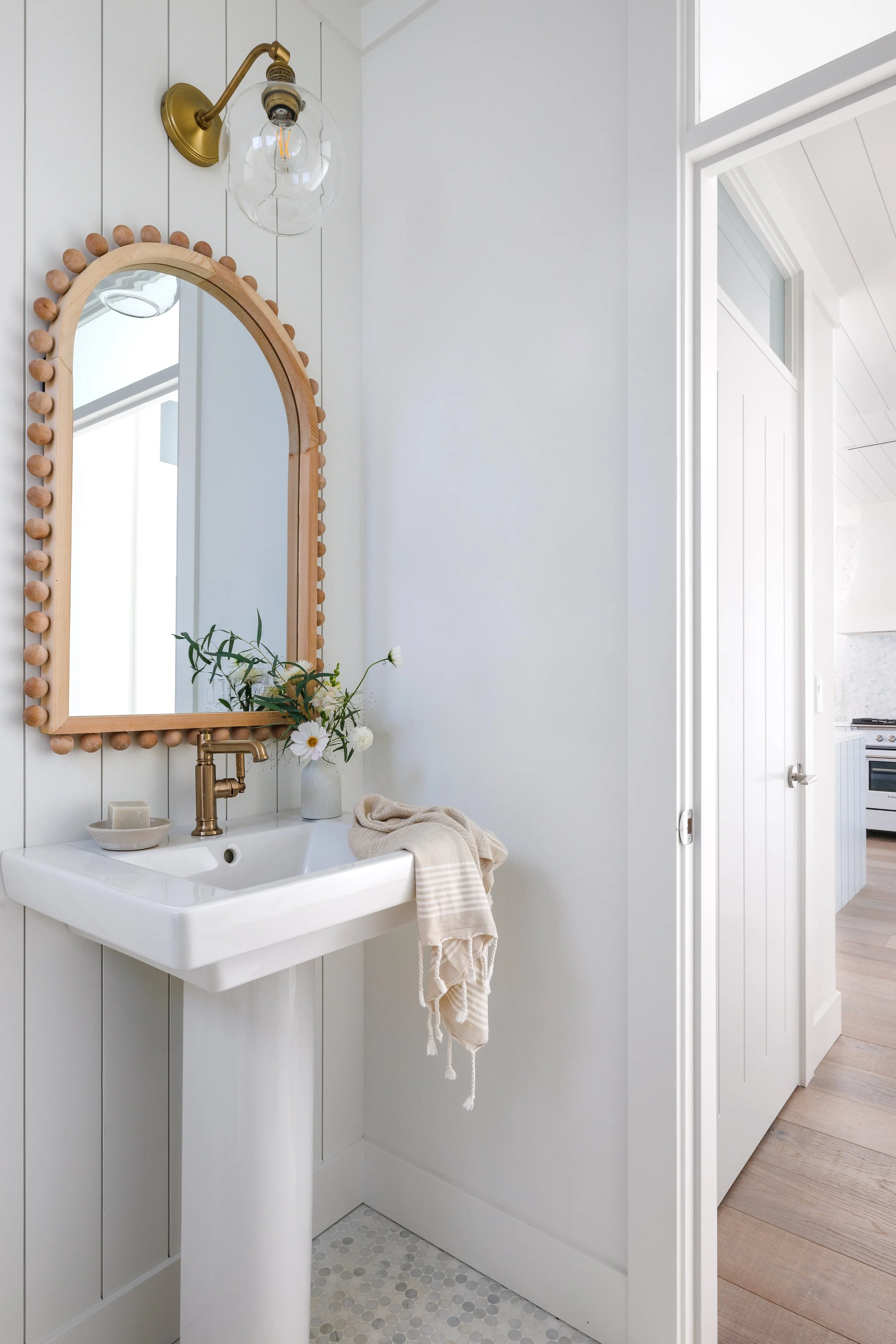Washroom with white porcelain pedestal sink, decorative wood mirror above and glass sconce.