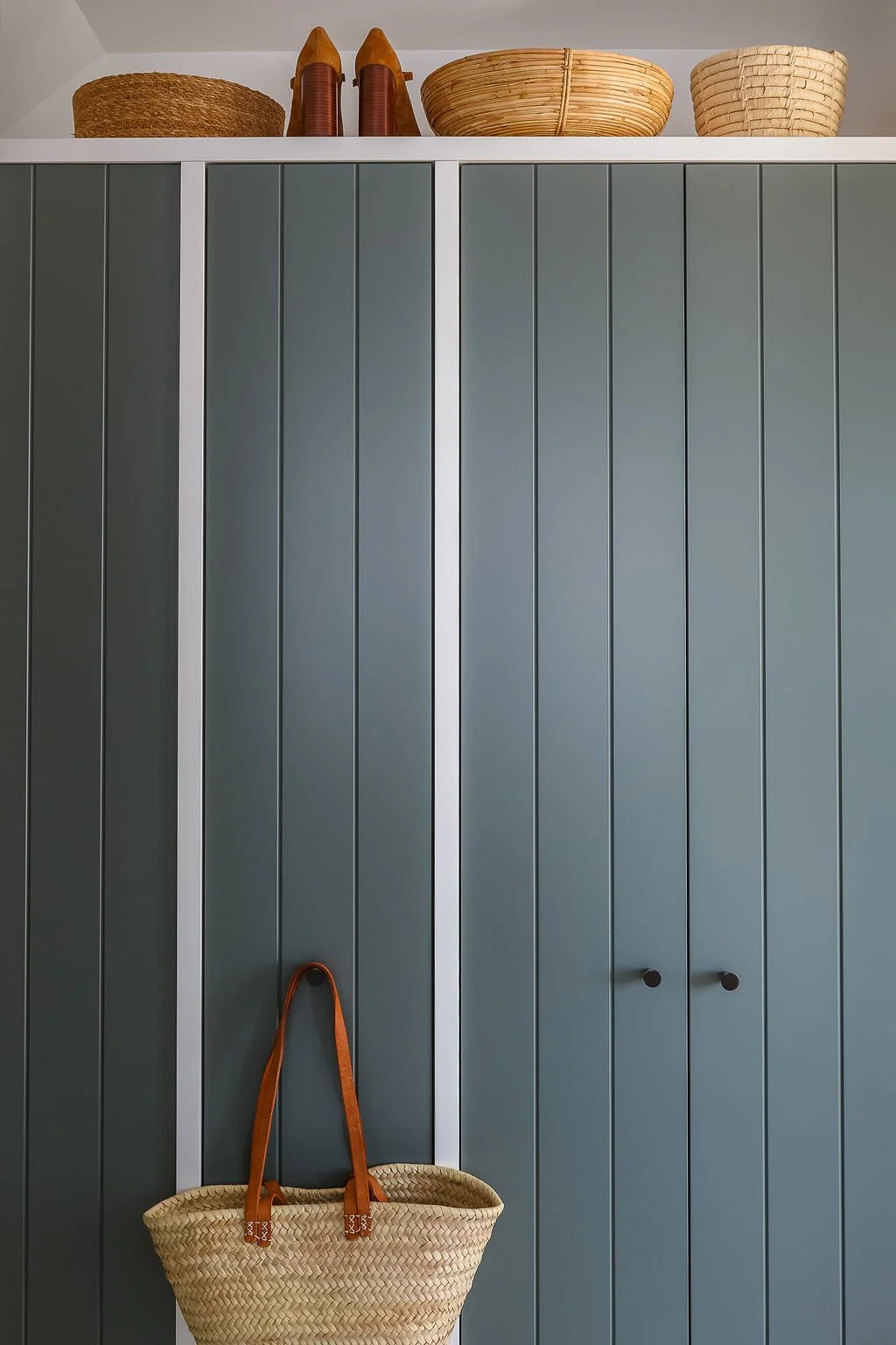 Green and white wardrobe cabinetry with woven baskets and leather shoes on top of cabinetry.