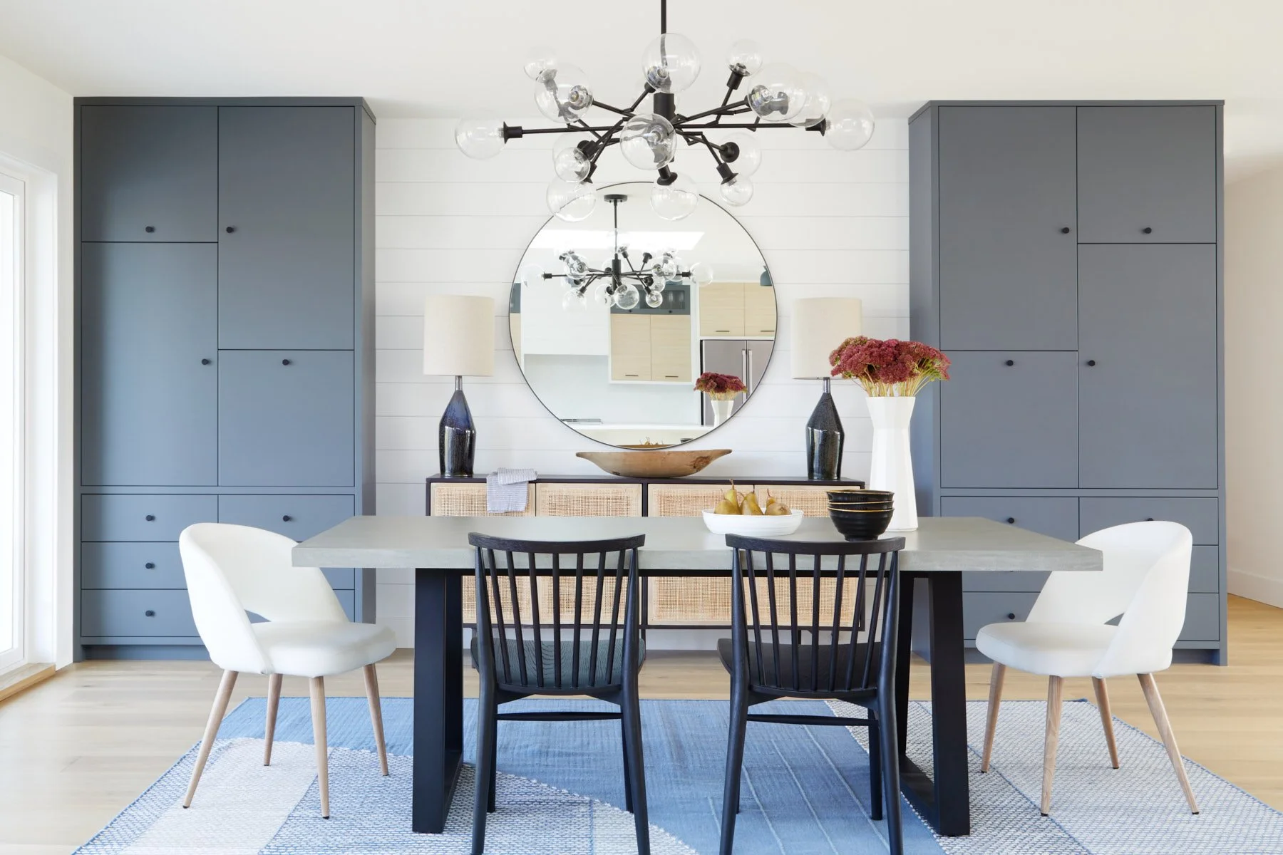 Photo of dining table and chair with blue cabinetry and mirror behind table, decor on table.