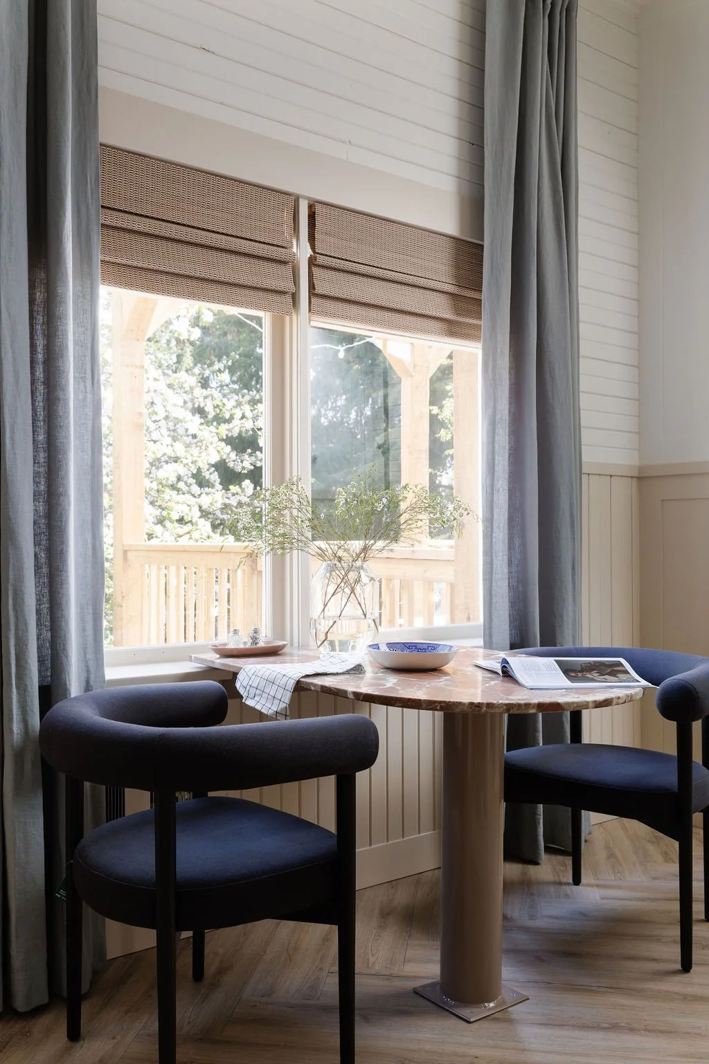 Two chairs at rounded marble bistro table in front of window looking out to apple tree.