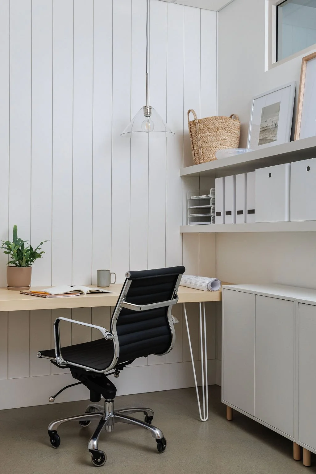 Photo of stylish white office with wood desk top and floating shelving with functional decor. 