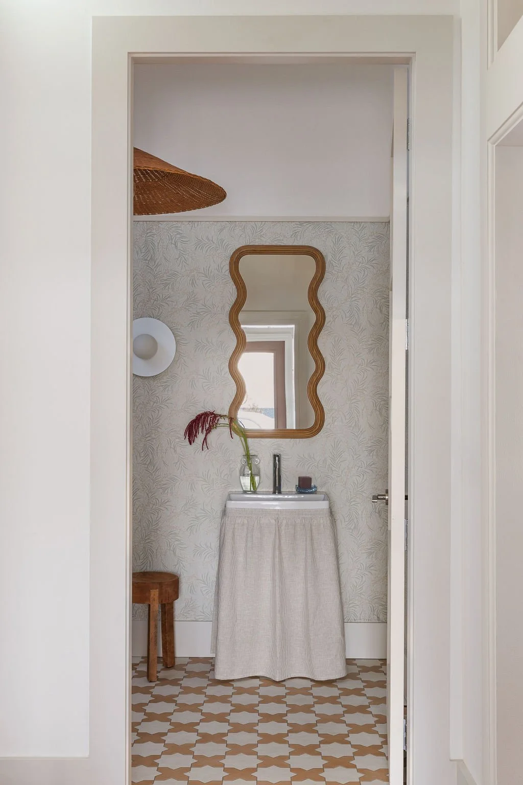 Looking through door into washroom with skirted vanity and wave mirror.