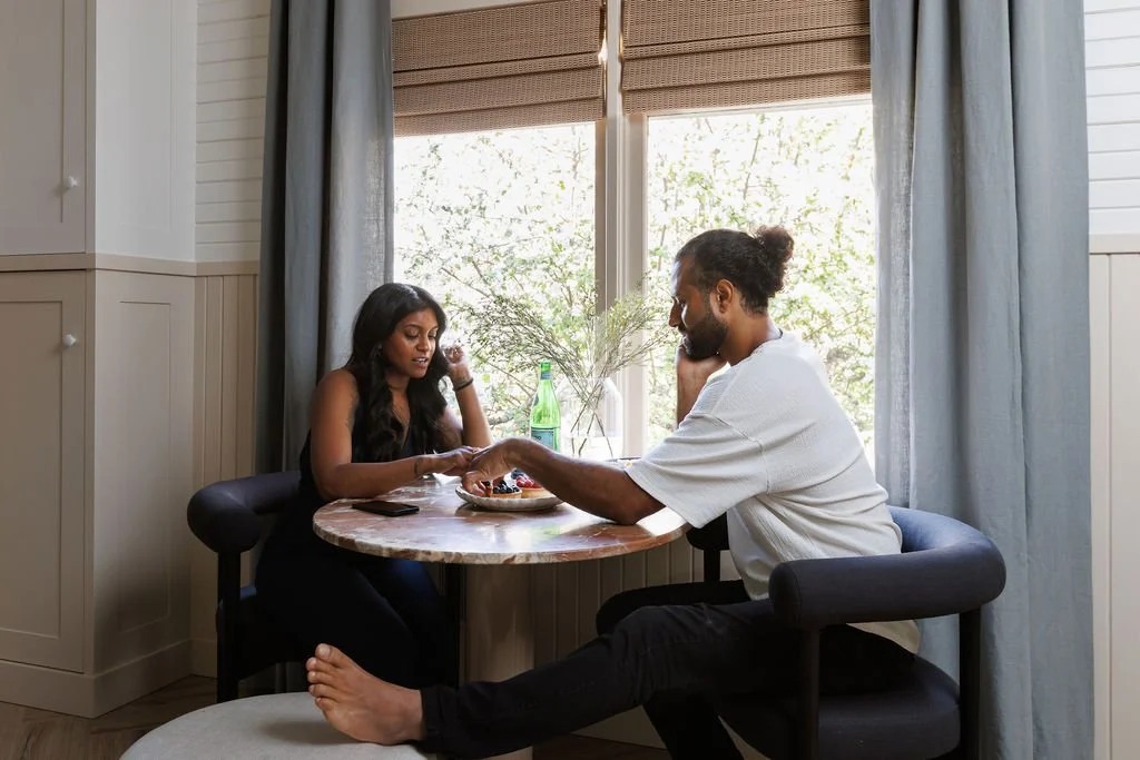 Siya and Rasila sitting at bistro table eating deserts next to sunlit window at Selby Hotel.