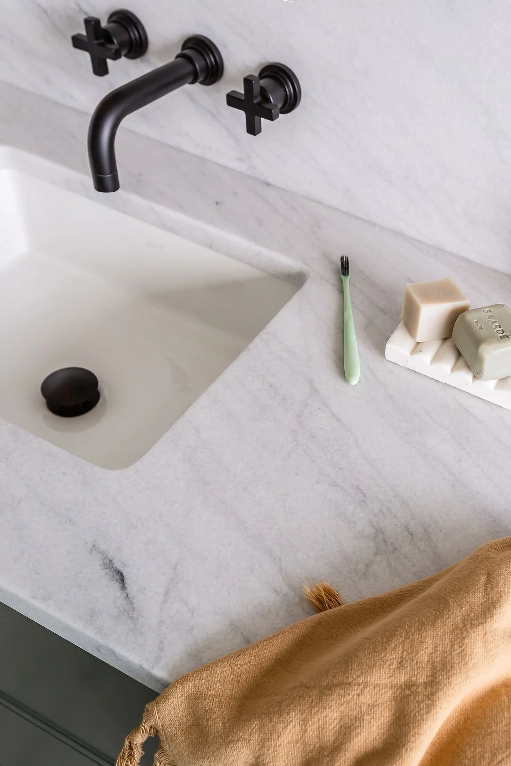 Close-up of marble vanity counter, a green toothbrush and soaps sitting on marble ribbed soap dish.