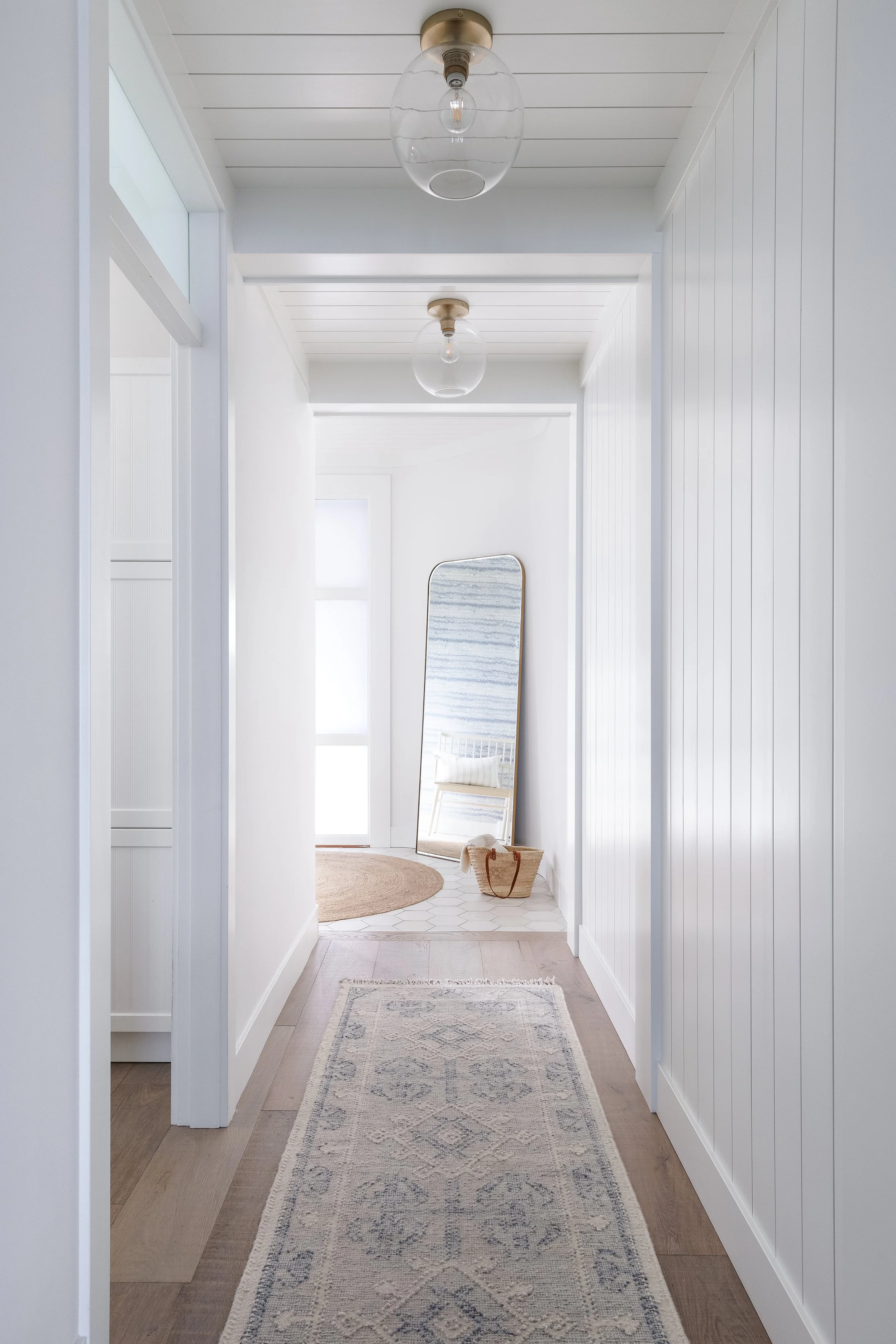 Hallway with rug looking towards mirror in sun-lit entry.