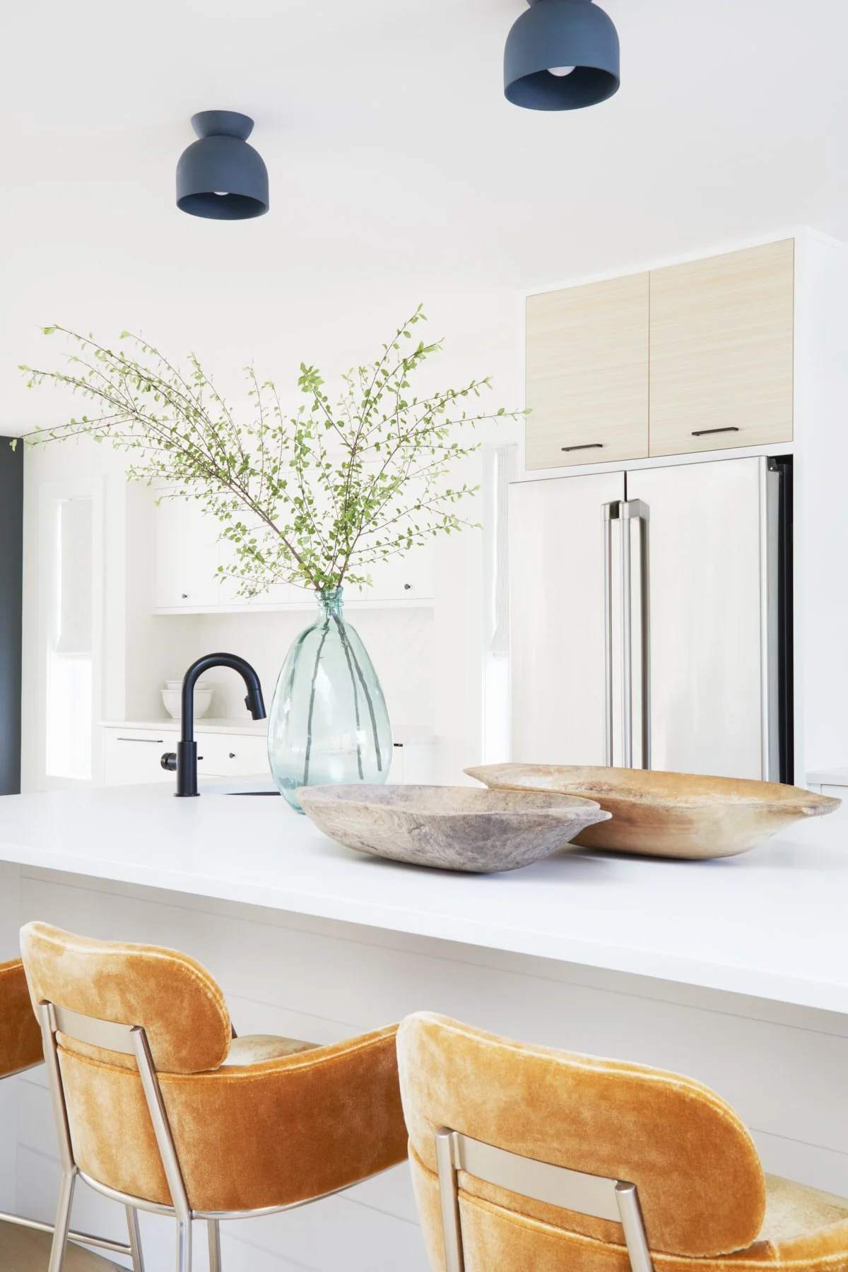 Close-up photo of kitchen island with gold velvet bar stools, wood decor and glass vase with branch greenery.
